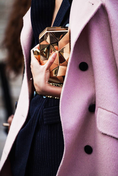 Détail d’un manteau rose porté sur un ensemble marine, avec une pochette dorée